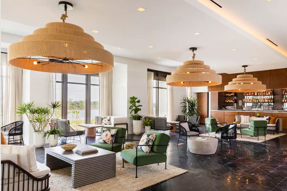 Contemporary hotel lounge with wooden pendant lights, green seating, bar, and expansive windows