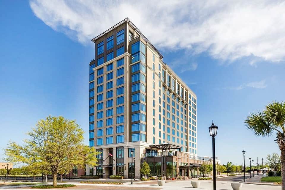 Contemporary beige hotel building with blue-trimmed windows and ground-level shops