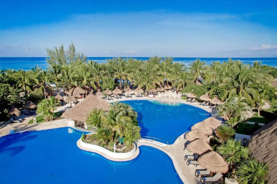 Aerial view of beachfront resort with palm trees, curved pools, and ocean