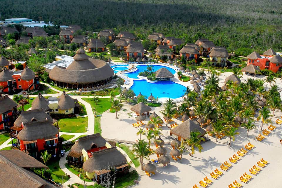 Aerial view of all-inclusive resort with thatched-roof buildings and blue pool