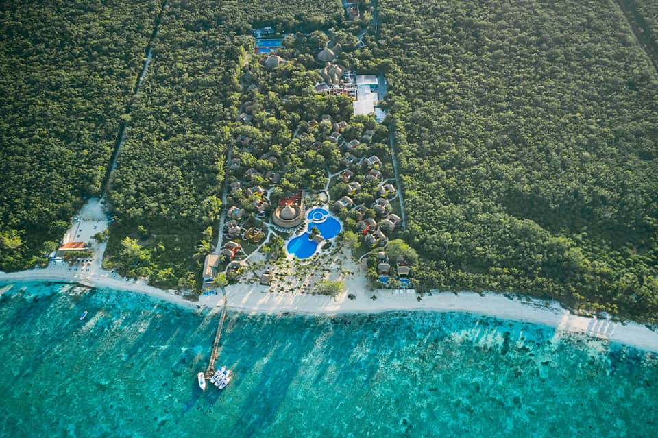 Aerial view of beachfront resort nestled in dense jungle with pools and turquoise waters