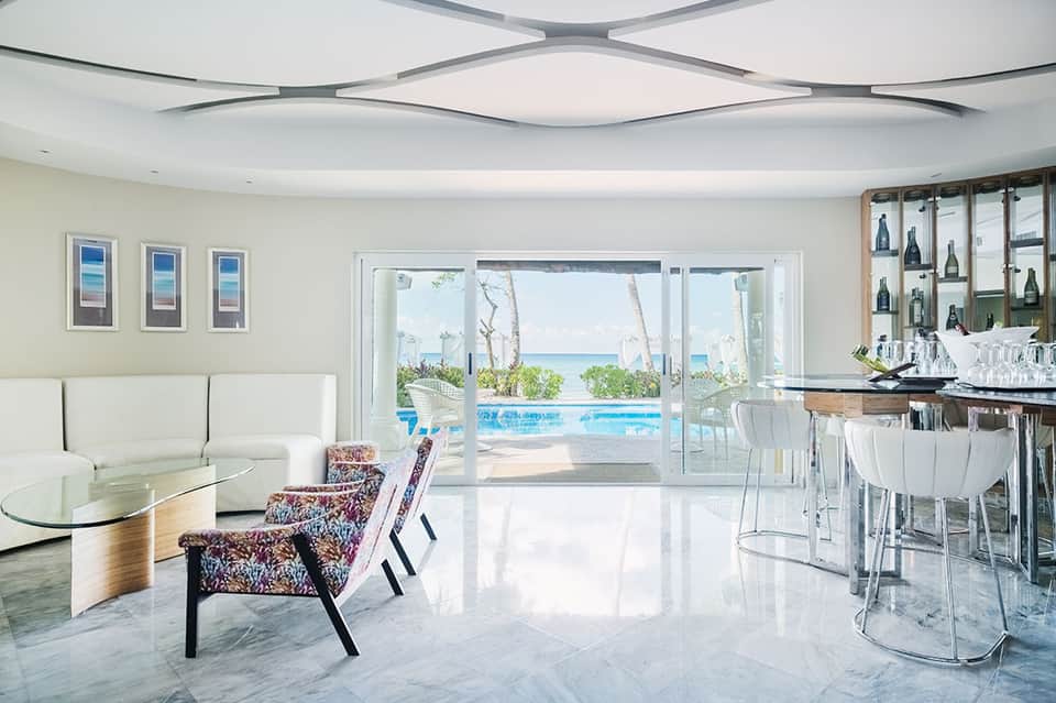 Luxury beachfront lounge with bar, seating, pool view, and ocean vista through glass doors