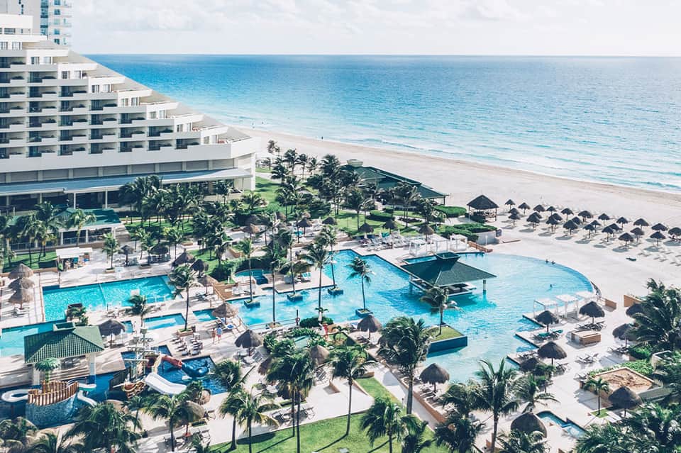 Aerial view of beachfront resort with large pool, palm trees, and ocean access