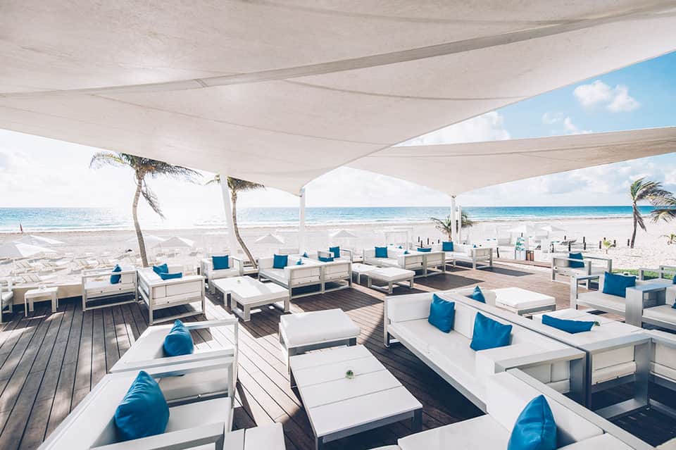 Beachfront lounge area with white daybeds, blue pillows, sailcloth canopy, and ocean views