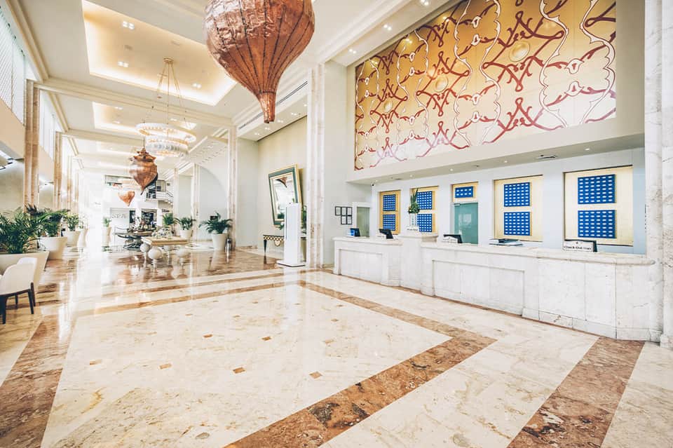 Luxurious hotel lobby with marble floors, decorative pendant lights, and artistic wall installations