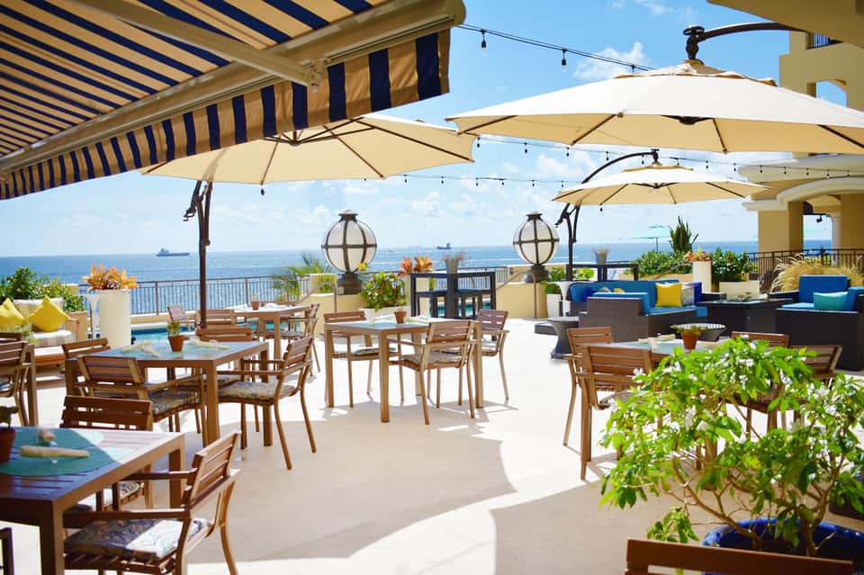 Oceanfront terrace with dining tables, umbrellas, and striped awnings overlooking the sea