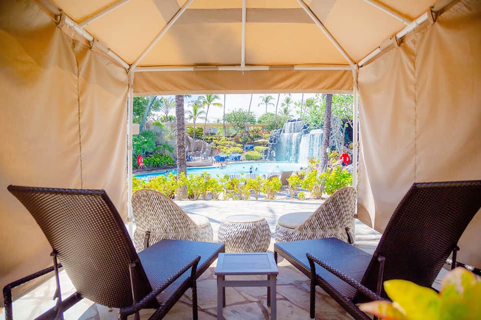 Glamping tent interior with comfortable seating overlooking a waterfall and tropical pool