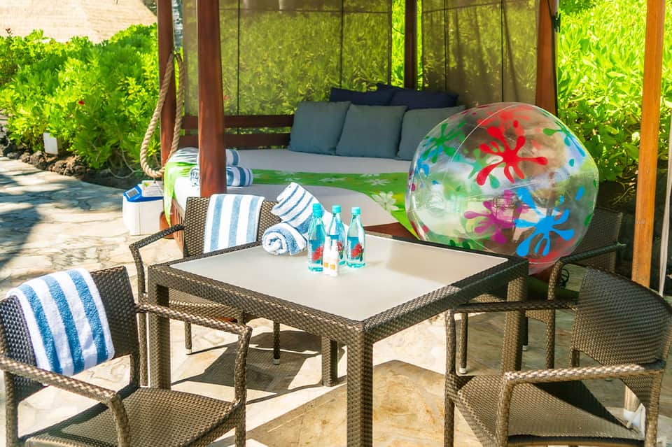 Beachside gazebo lounge with striped cushions, colorful inflatable ball, and ocean view access