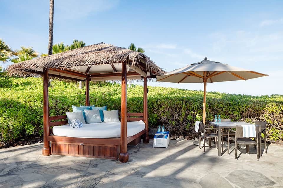 Beachfront cabana with thatched roof bed, white linens, blue pillows, and ocean view