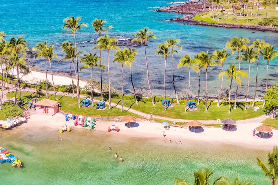 Aerial view of pristine beach with palm trees, turquoise water, and colorful beach umbrellas and loungers