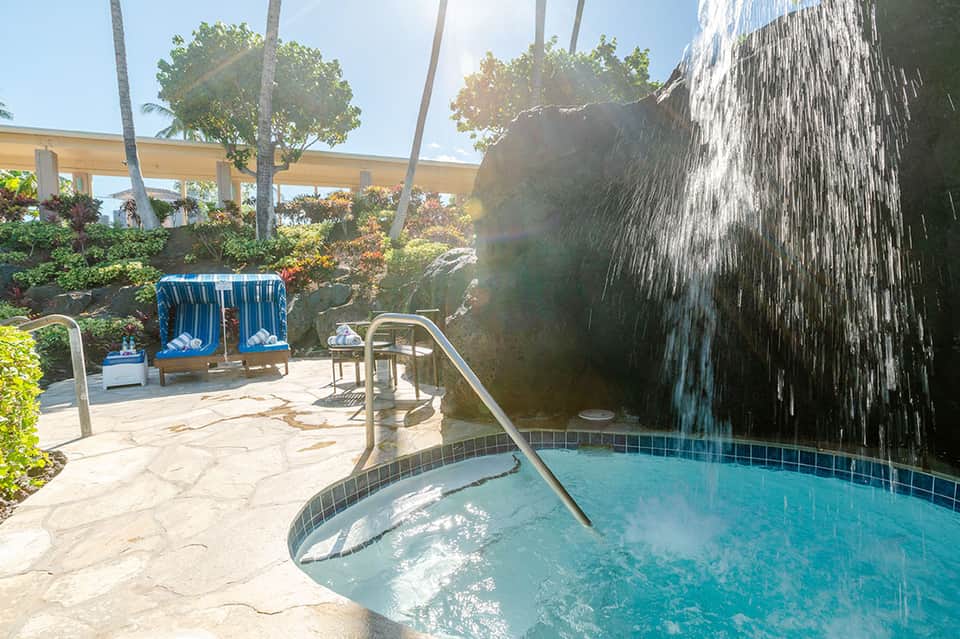 Hot spring pool with waterfall feature, lounge chairs, and palm trees