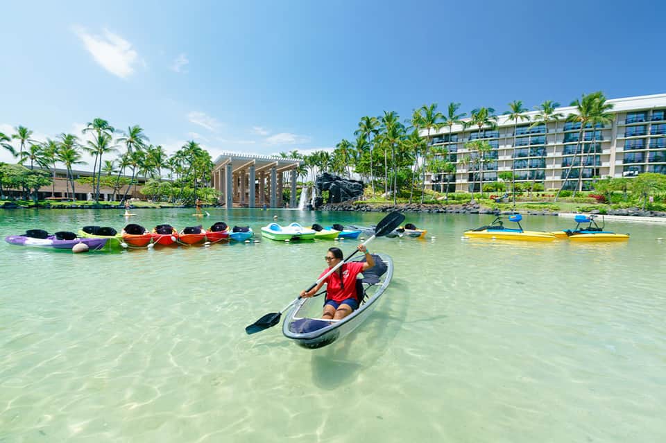 Tropical resort lagoon with colorful kayaks, palm trees, and guest paddling in clear water