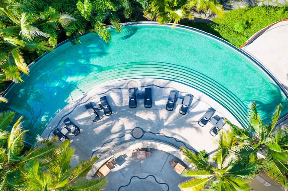Aerial view of curved resort pool surrounded by palm trees and lounge chairs