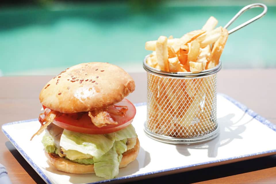 Gourmet burger with lettuce and tomato, served with crispy fries in wire basket by pool
