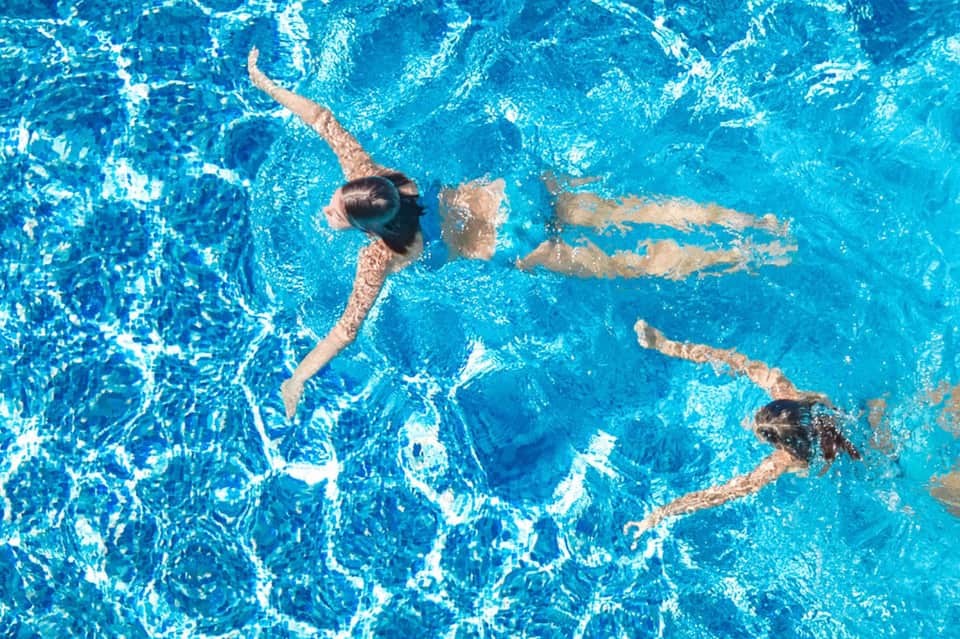 Aerial view of swimmers doing freestyle laps in bright turquoise pool water