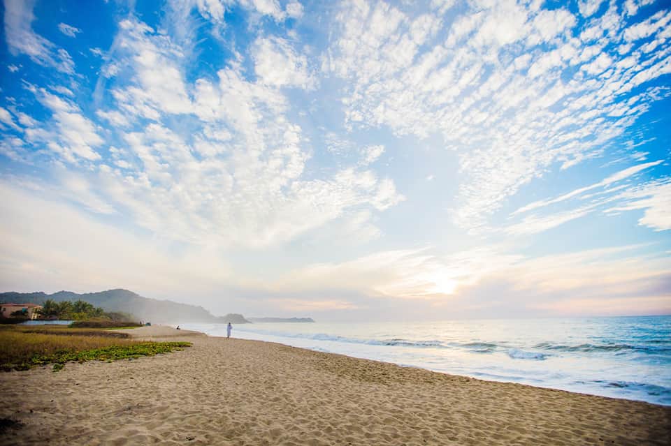 Scenic beach at sunset with mountains, waves, and dramatic sky