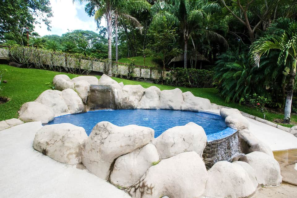 Natural hot spring pool surrounded by large white rocks in tropical garden setting