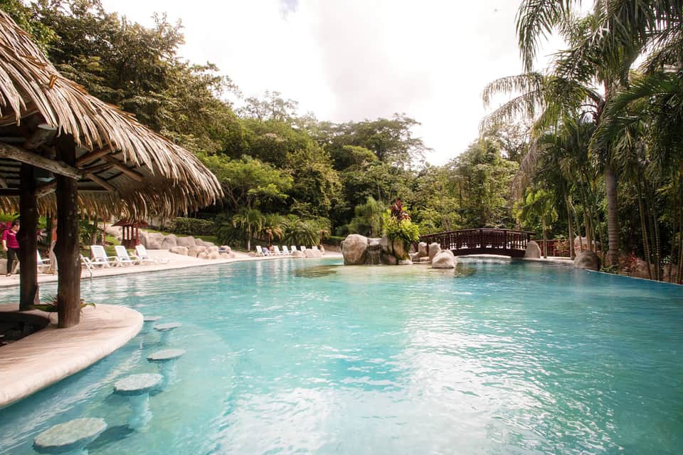 Crystal-clear turquoise lagoon pool with thatched-roof cabanas and lush tropical vegetation