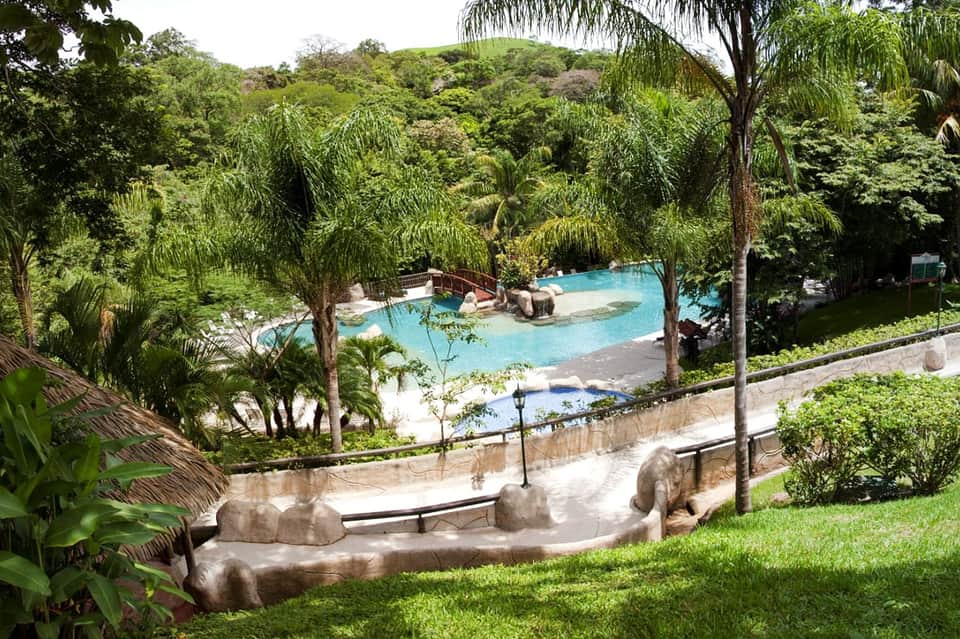 Resort hot spring pool surrounded by lush tropical vegetation and palm trees