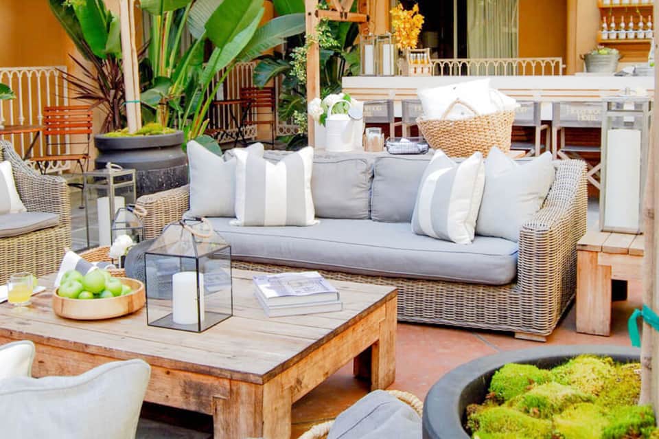 Outdoor patio lounge with wicker furniture, cushions, and tropical plants