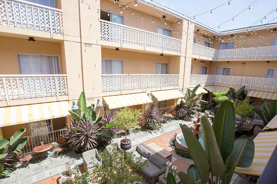 Courtyard with tropical plants, lounge seating, and multi-story hotel building with white railings