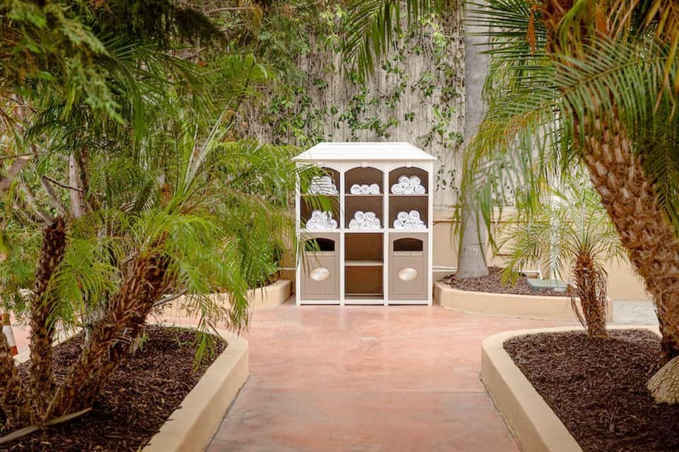 White towel storage cabinet in a tropical courtyard surrounded by palm trees and lush vegetation