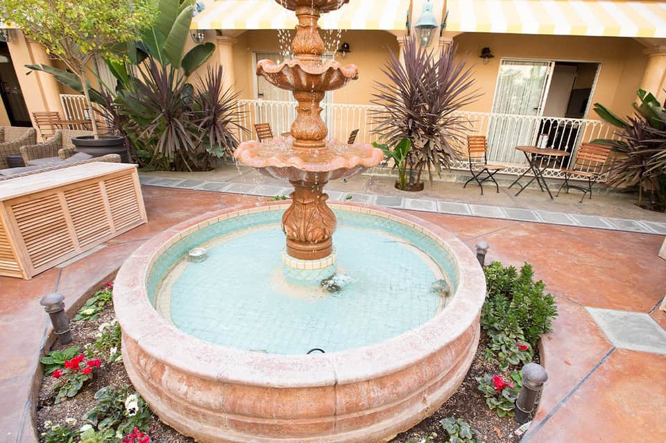 Courtyard with decorative fountain, terracotta tile flooring, and beige building facade