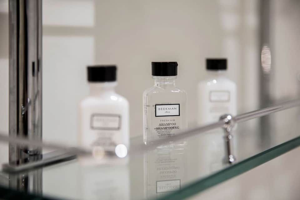 Bathroom counter displaying luxury Beekman toiletries in glass bottles with mirror reflection