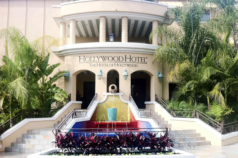 Historic Hollywood Hotel facade with palm trees and colorful fountain courtyard entrance