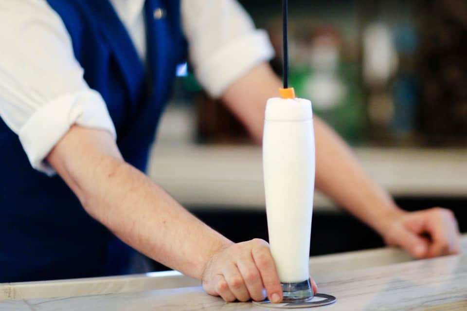 Bartender pouring white cocktail into tall glass with citrus garnish at resort bar