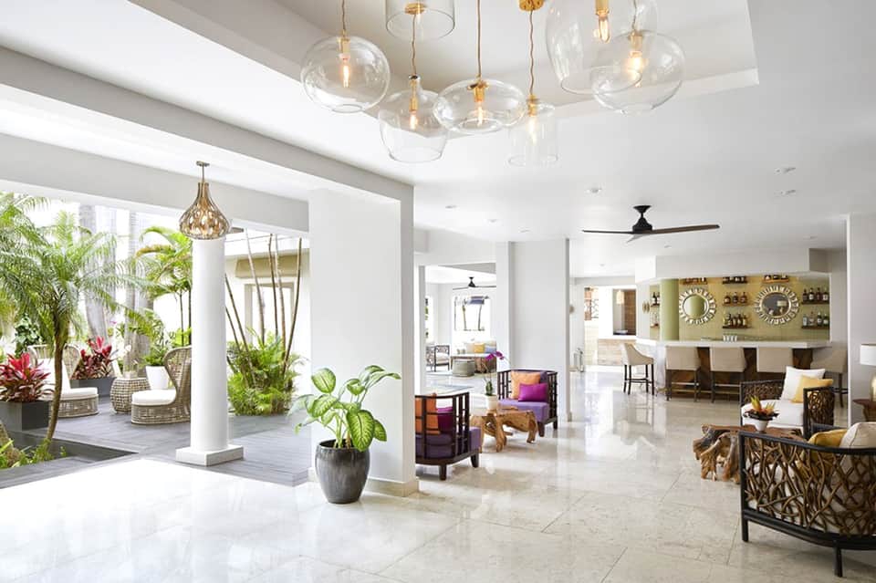 Spacious hotel lobby with pendant lights, tropical plants, and modern seating areas