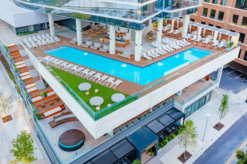 Aerial view of multi-level resort with two bright blue pools, white lounge chairs, and surrounding brick buildings