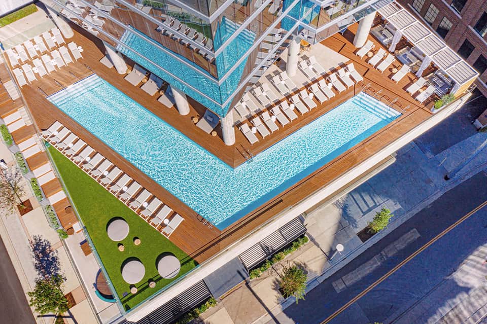 Overhead view of resort pool deck with wooden loungers, turquoise lap pools, and green lawn areas