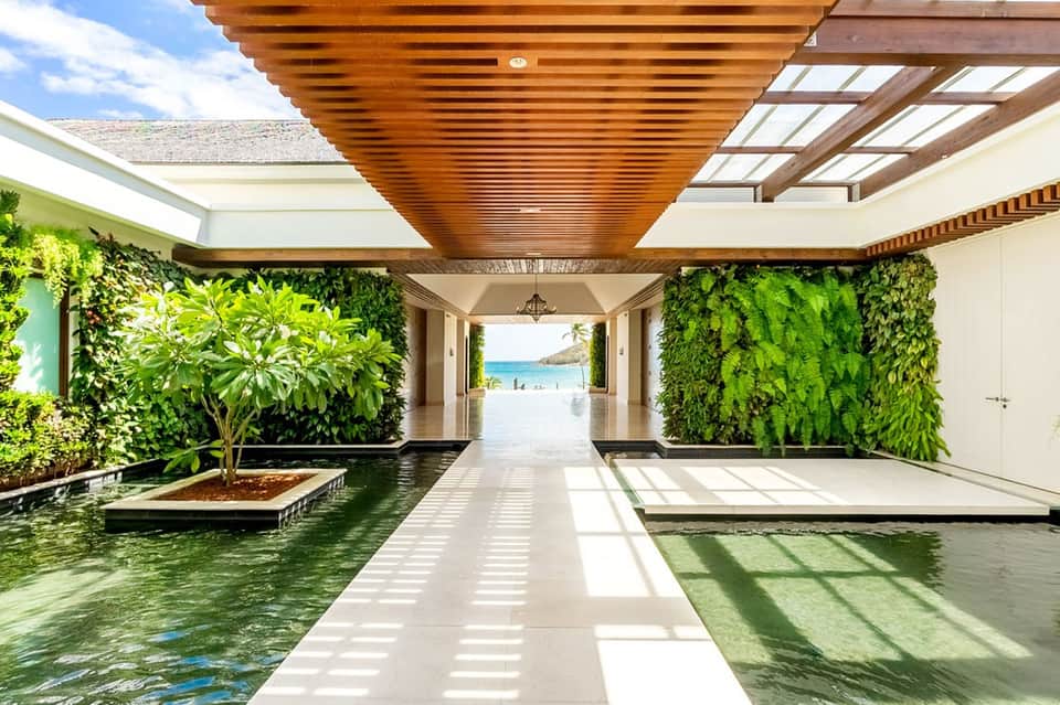 Modern covered corridor with wooden ceiling, living plant walls, and waterway leading to ocean view
