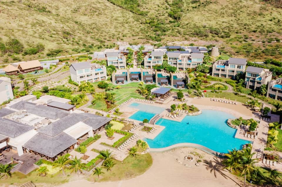 Aerial view of beachfront resort with multiple pools, buildings, and lush grounds on hillside