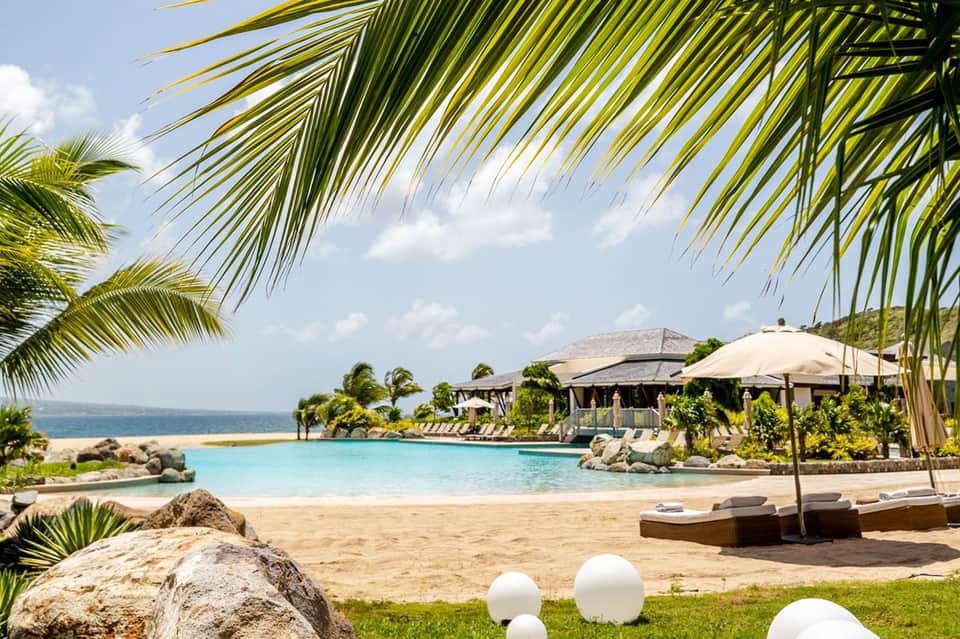 Tropical resort beach lagoon with palm trees, white umbrellas, and sandy shoreline