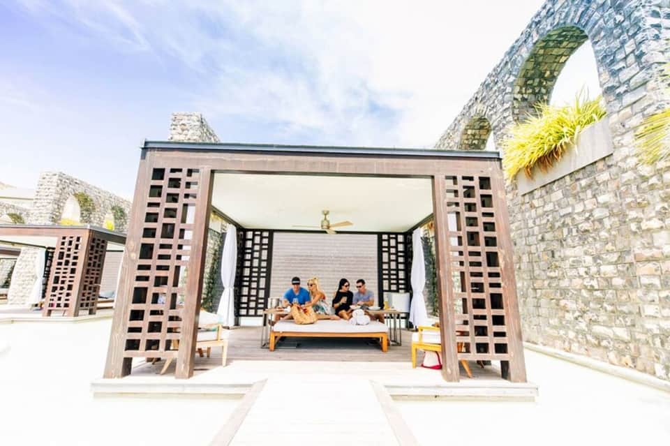 Outdoor pavilion with wooden lattice doors and arches, guests relaxing on a daybed under stone archways