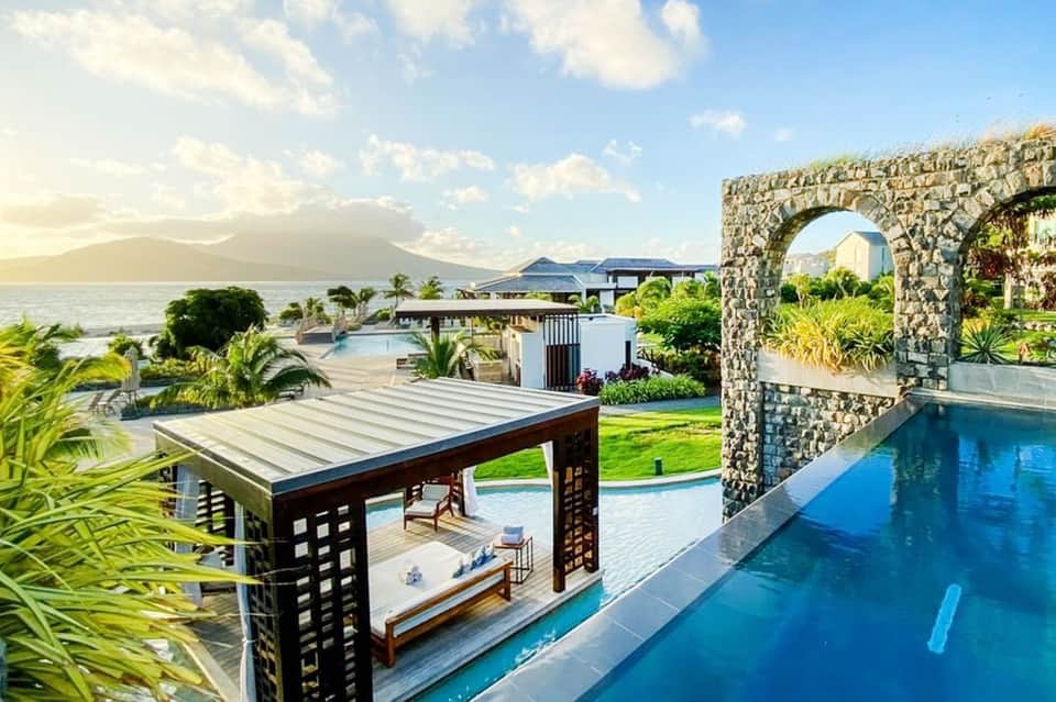 Oceanfront resort with infinity pool, stone archway, and mountain views across the water