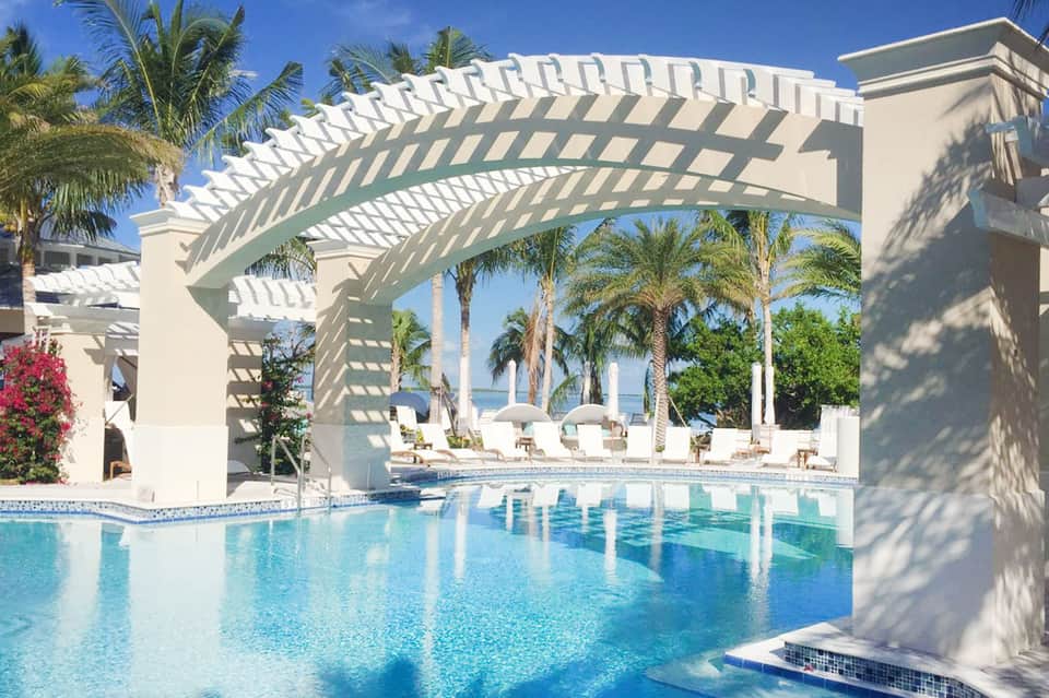 Luxury beachfront resort pool with white pergola, palm trees, and ocean view
