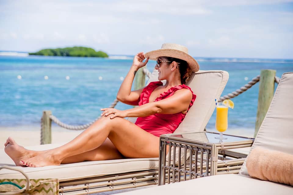 Woman in pink swimsuit relaxing on beach lounge chair with ocean and island backdrop
