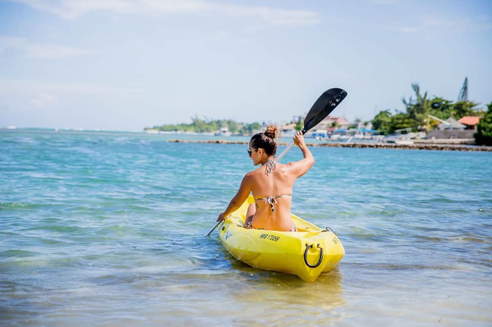 Woman paddling yellow kayak in clear turquoise ocean water near tropical shoreline
