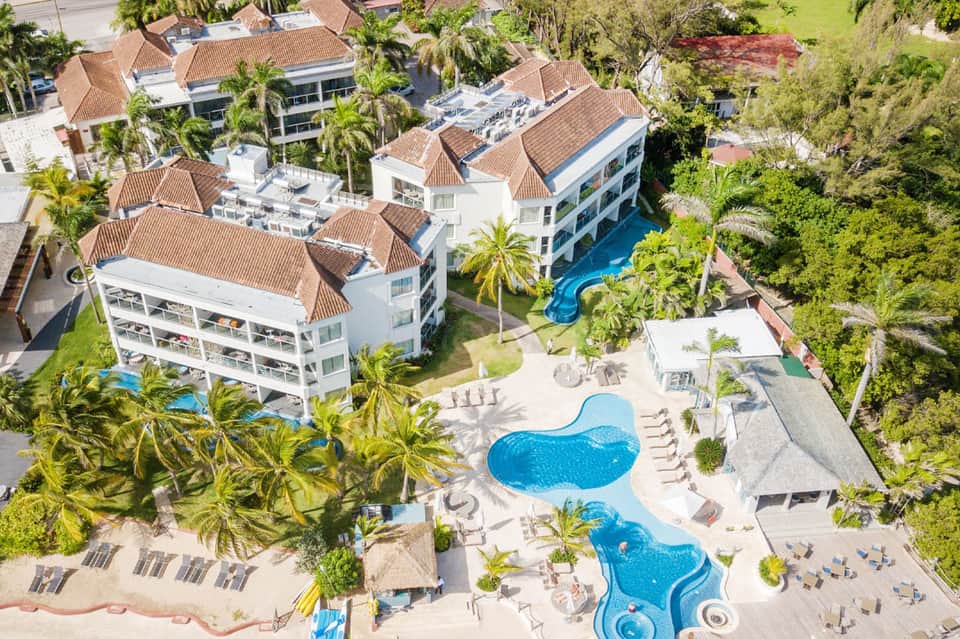 Aerial view of beachfront resort with multiple pools, palm trees, and white buildings