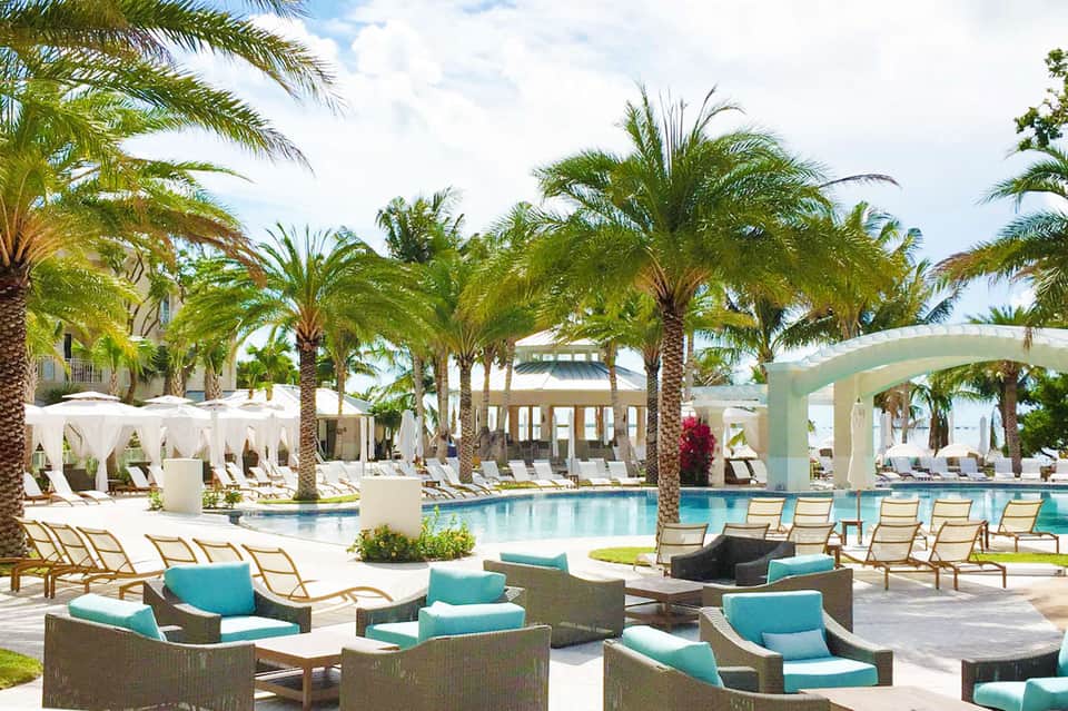 Luxury resort pool surrounded by palm trees, white cabanas, and lounge chairs with turquoise cushions