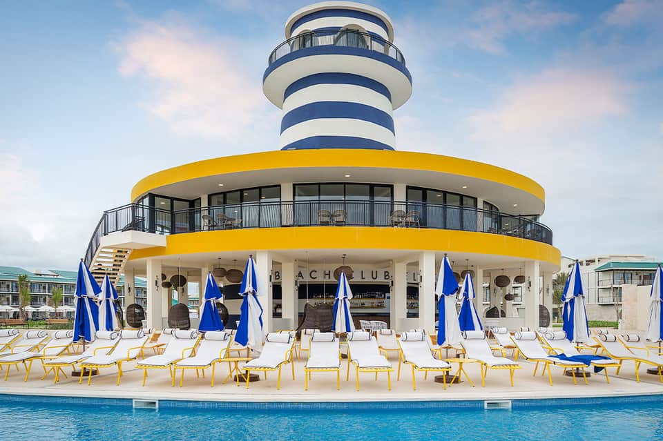 Beachfront yacht club with striped umbrellas, lounge chairs, and distinctive striped tower architecture