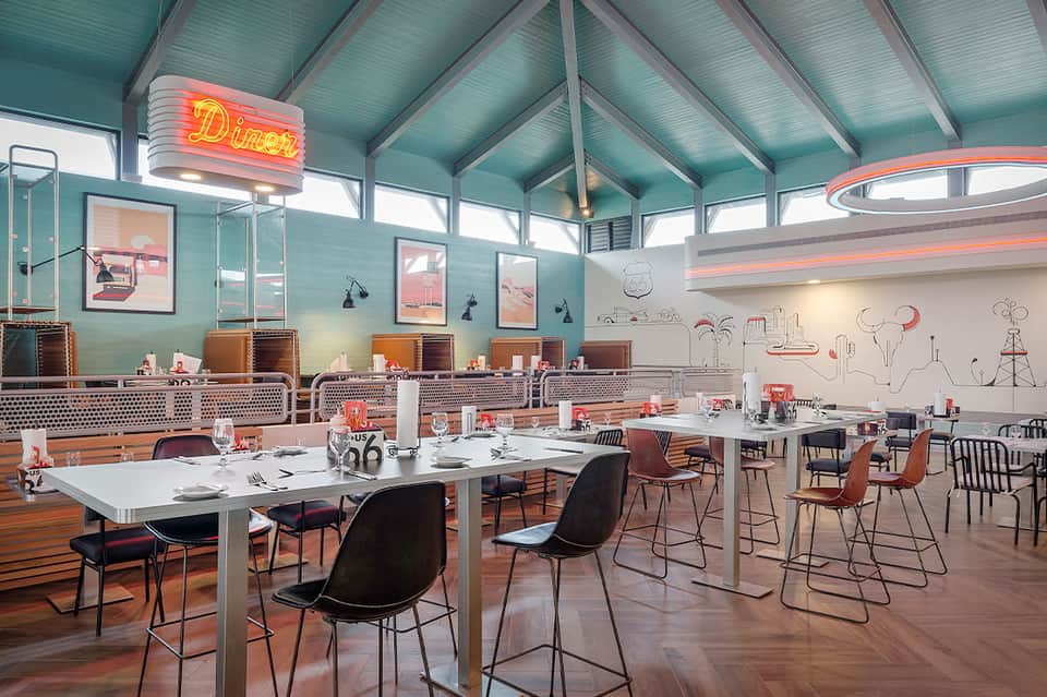 Retro diner interior with turquoise walls, neon sign, and dining tables