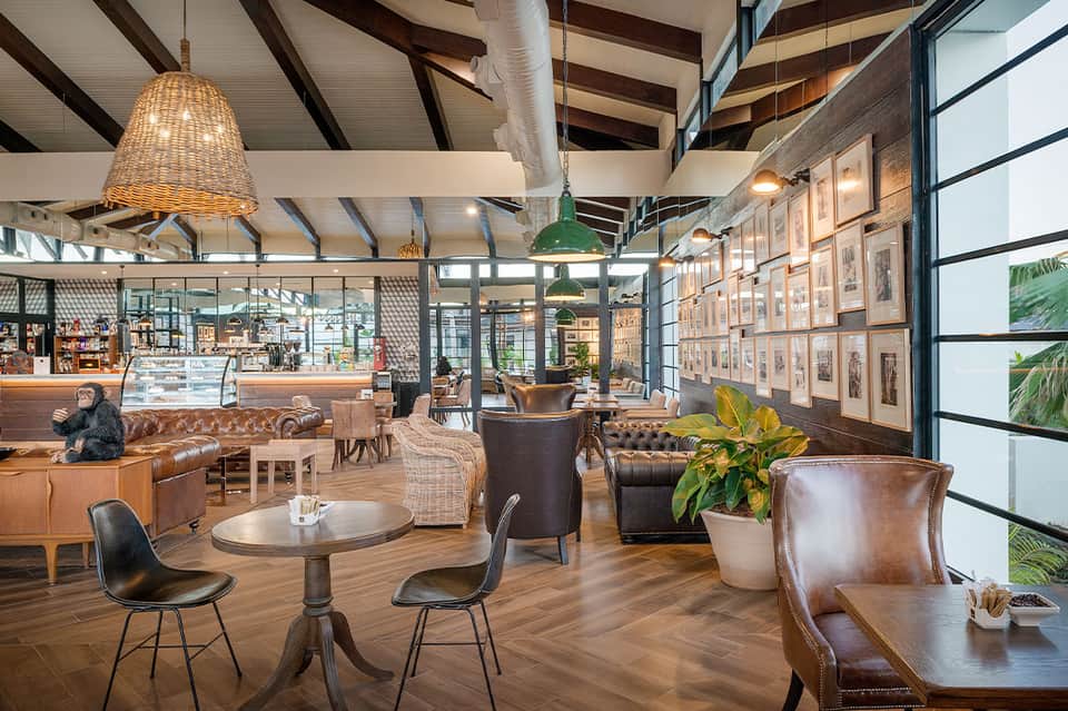 Modern hotel lobby with leather seating, woven pendant lights, exposed beams, and framed artwork on walls