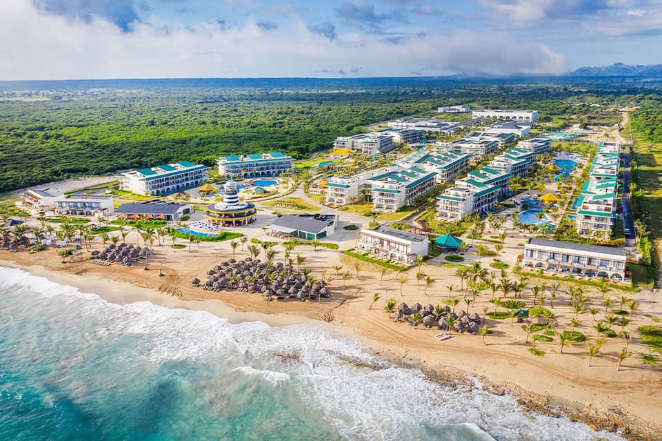 Aerial view of a beachfront resort complex with multiple pools and buildings nestled in lush tropical landscape