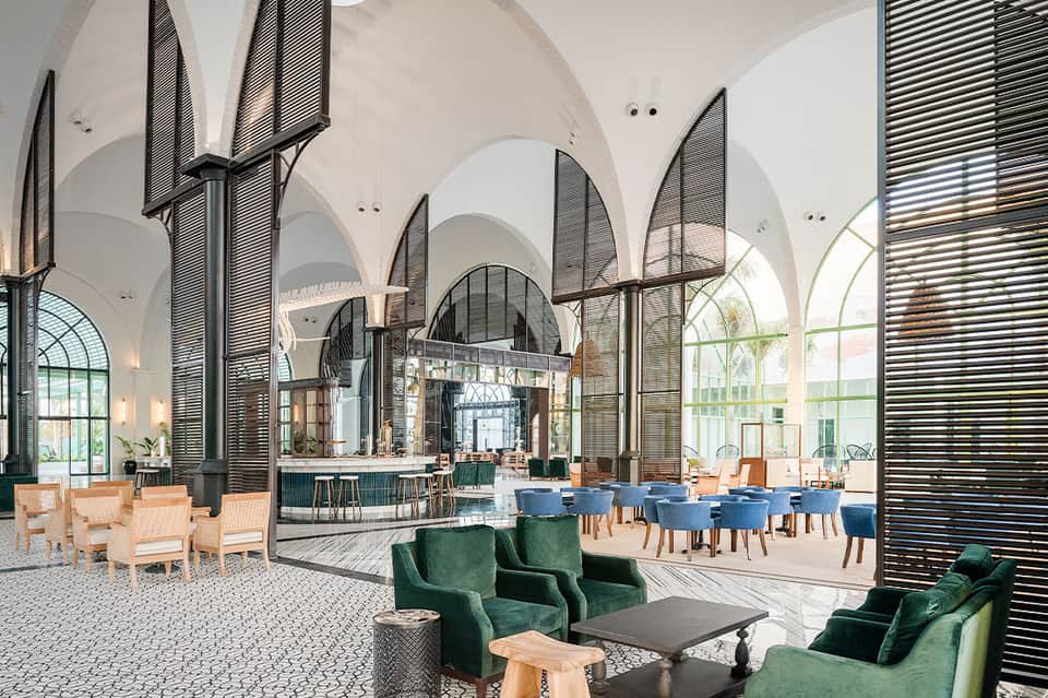 Modern hotel lobby with arched white ceilings, green velvet seating, and large windows