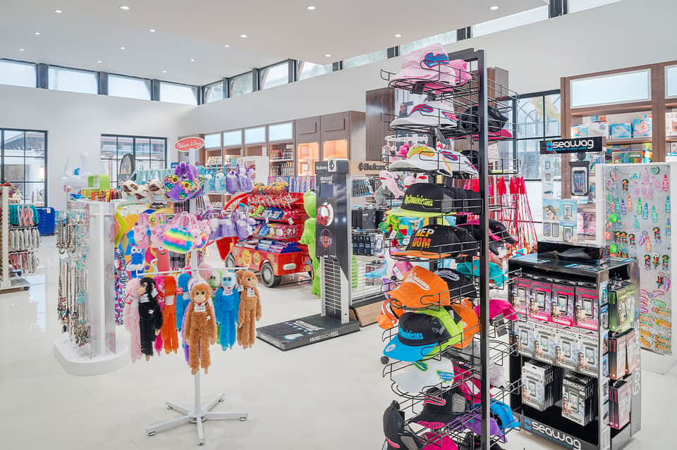 Bright retail store interior with colorful merchandise displays, dolls, and beach/water sports equipment
