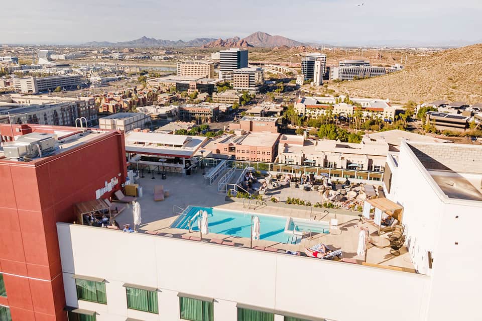 Rooftop pool and lounge area at desert resort with mountain views and surrounding urban landscape